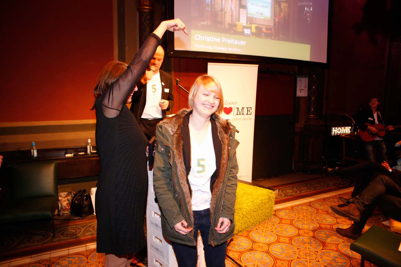 Chrissi steht vor einer Person, die auf die zeigt, und lacht