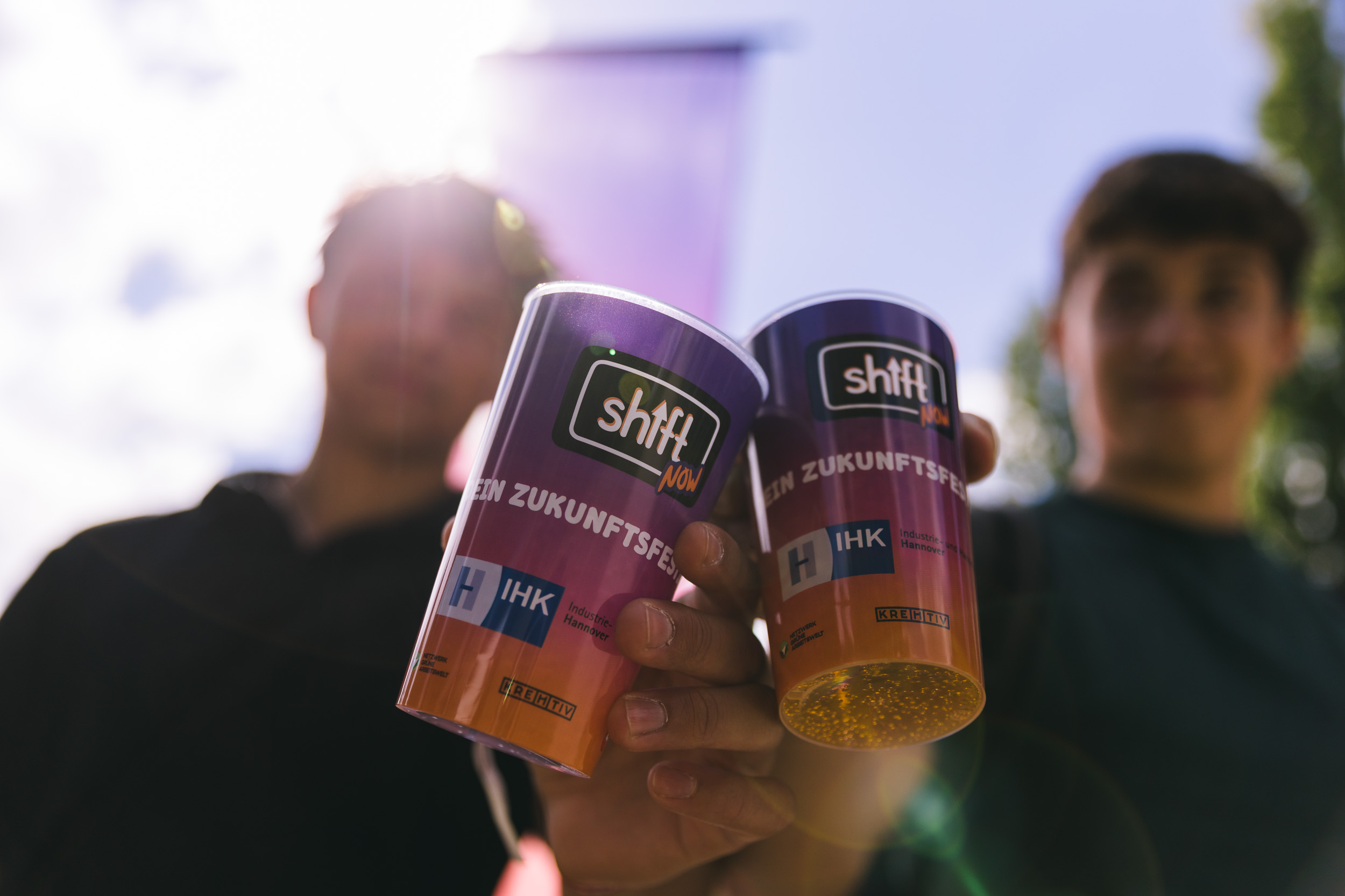 Zwei Jungen halten zwei gebrandetete SHIFT NOW Becher in die Kamera