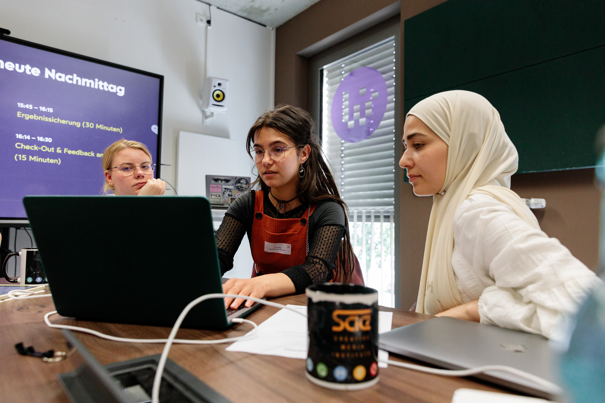 Drei Frauen sitzen vor einem Laptop und besprechen etwas.