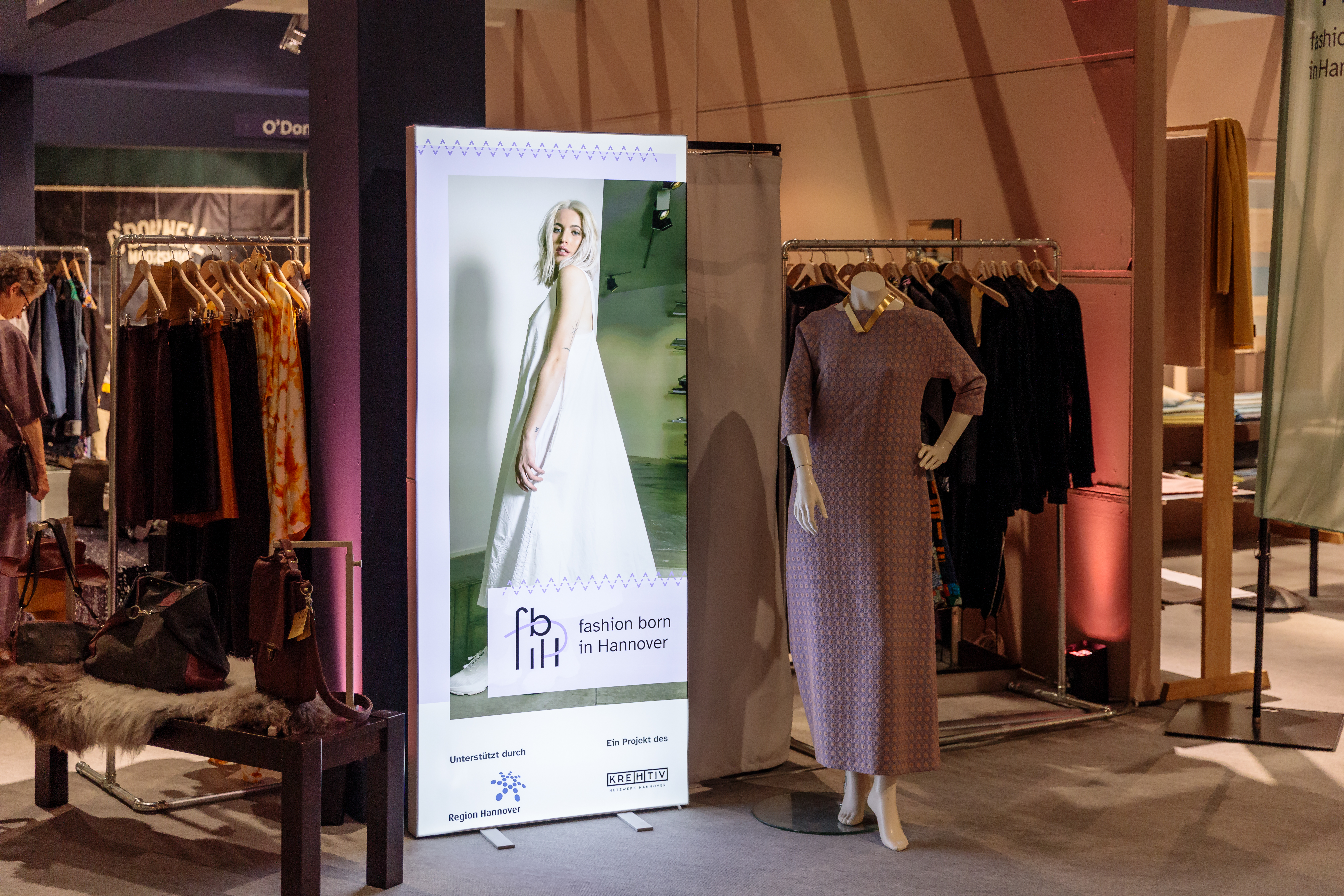 Mittig steht ein Pixlip Pop, darauf ist eine weiblich gelesene Person in einem weißen Kleid. Darunter steht "Fashion Born in Hannover", unterstützt durch Region Hannover, ein Projekt des kreHtiv Netzwerk Hannover.